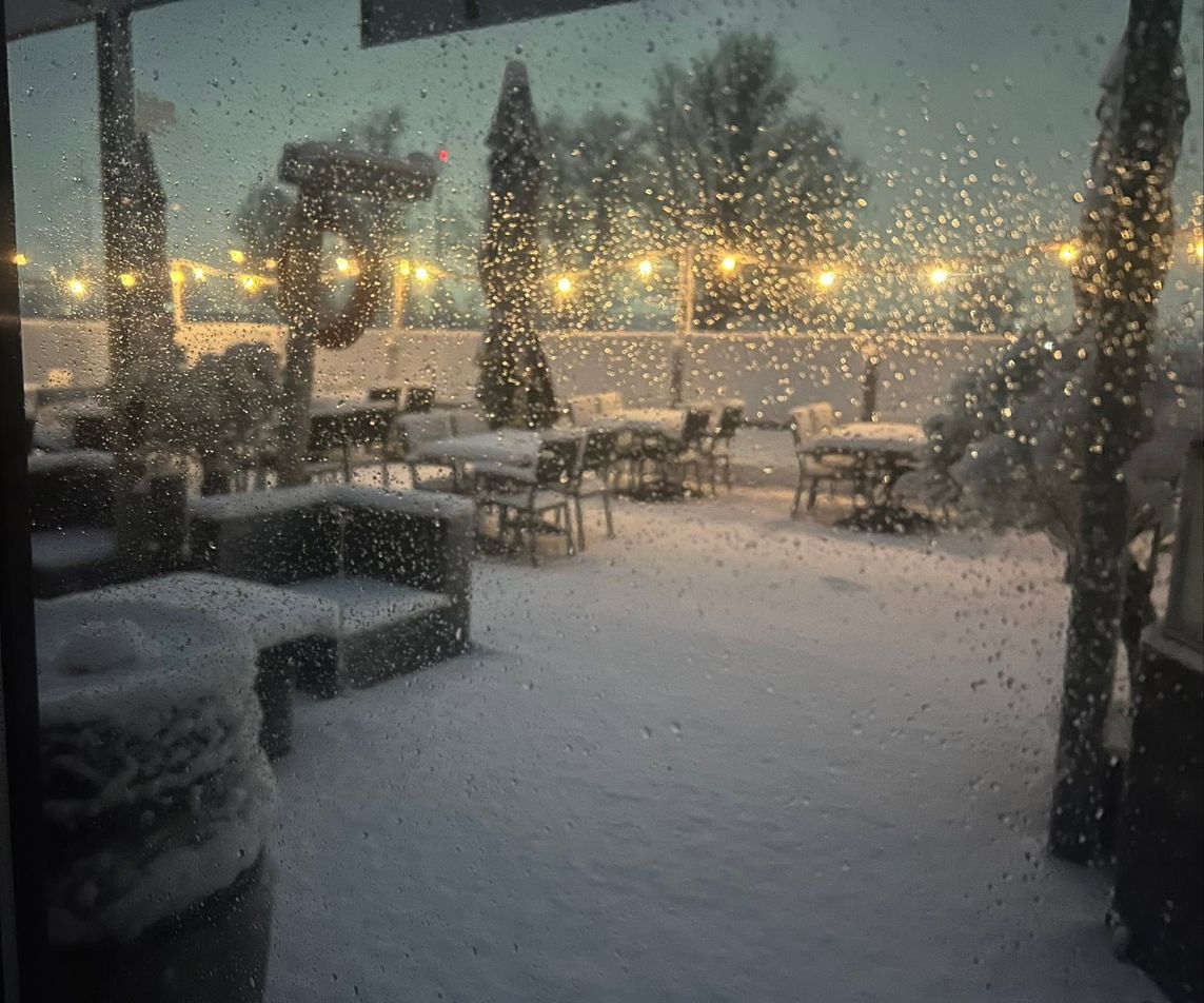 Het terras in de sneeuw met lichtjes, gezien door het raam van de zaal